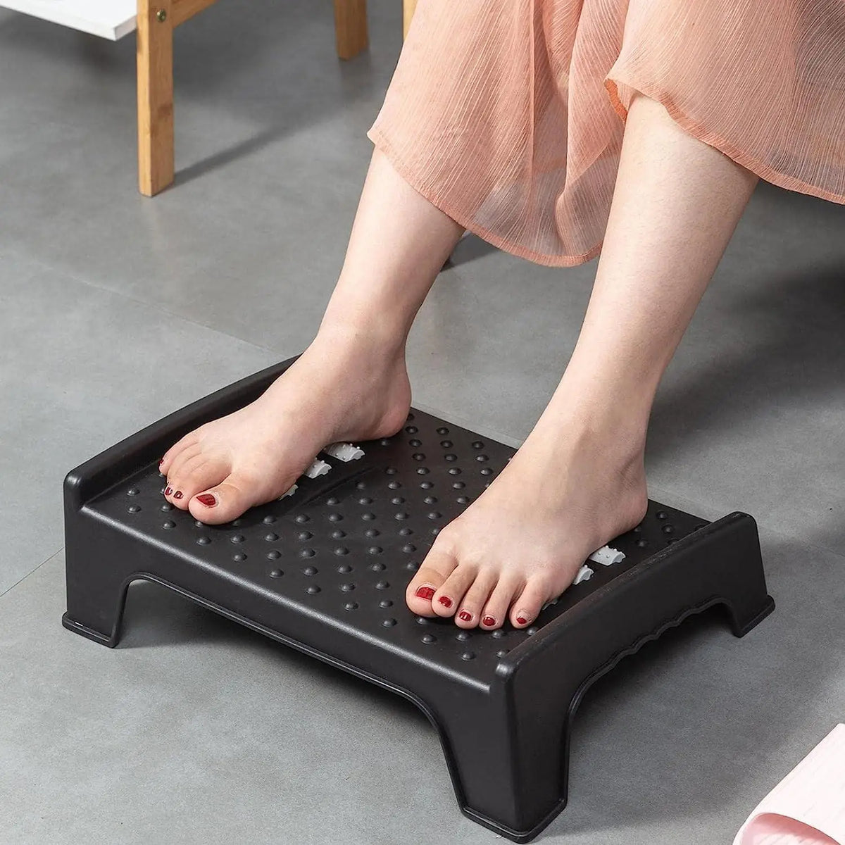 A plastic under-desk foot rest featuring integrated massage rollers and surface particles.