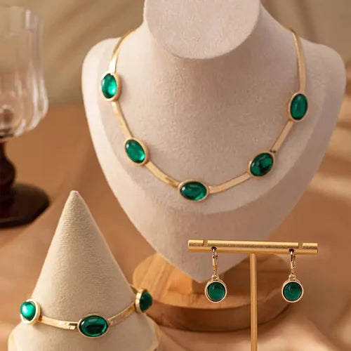 A necklace and bracelet set featuring oval green crystals set in gold-plated stainless steel.